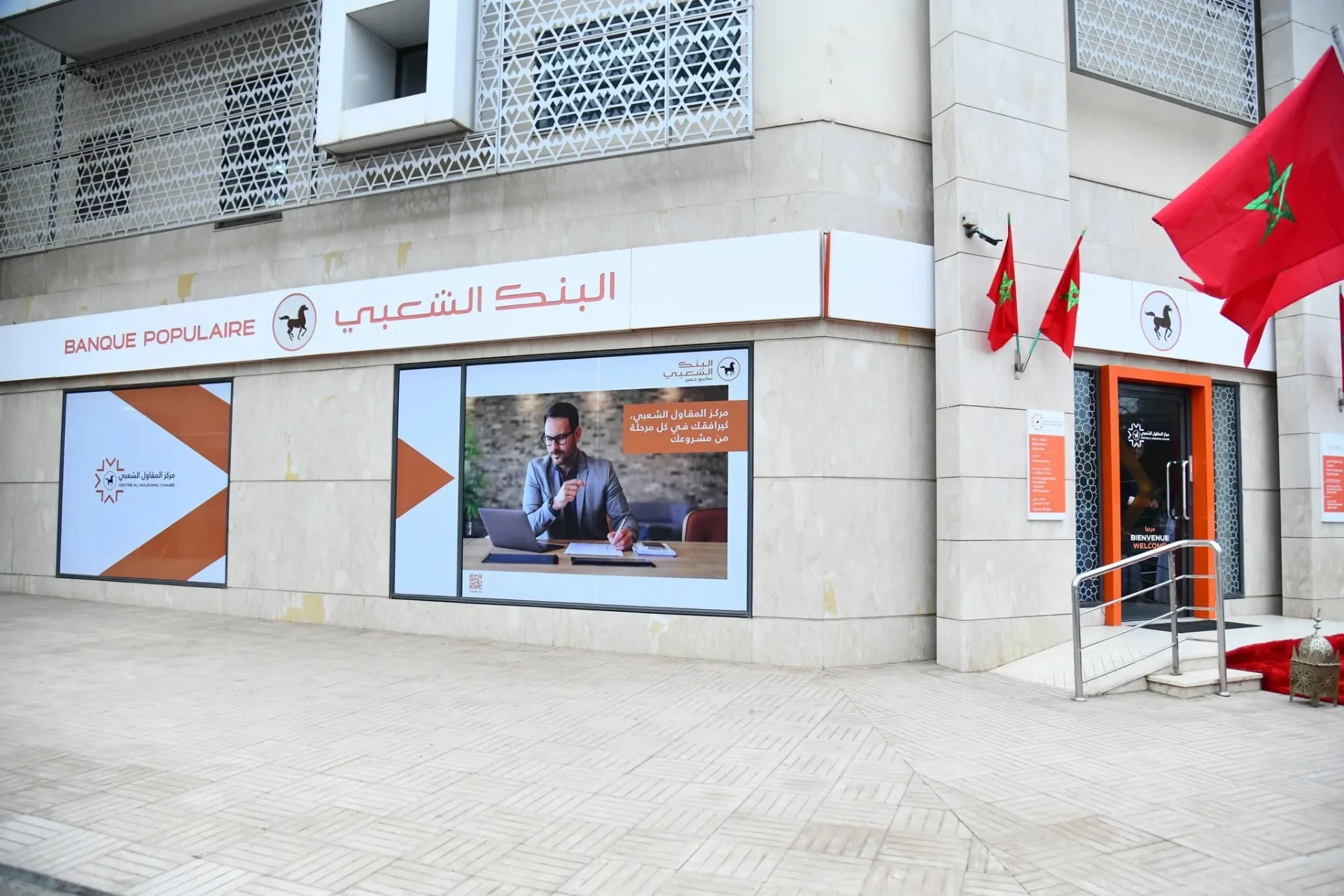 Façade d'une agence Banque Populaire au Maroc avec drapeaux marocains et vitrine publicitaire sur le financement immobilier